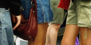 Fotograma en pla detall on es veuen diversos passatgers de peu al metro, destacant una bossa de mà gran de color granat.
