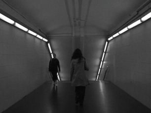 Una jove avança pels passadissos del metro de Barcelona, captada en blanc i negre, mentre la llum artificial dels fluorescents il·lumina el seu pas cap a les andanes.