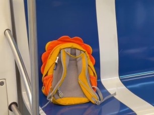 Una motxilla infantil taronja asseguda sola en un seient blau del metro de Barcelona