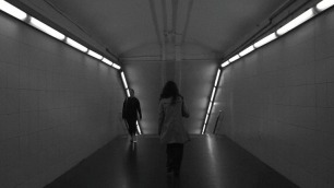 Una jove avança pels passadissos del metro de Barcelona, captada en blanc i negre, mentre la llum artificial dels fluorescents il·lumina el seu pas cap a les andanes.